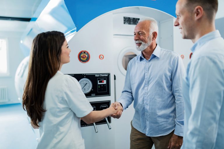 Happy senior patient and female doctor shaking hands after hyperbaric oxygen therapy at clinic.