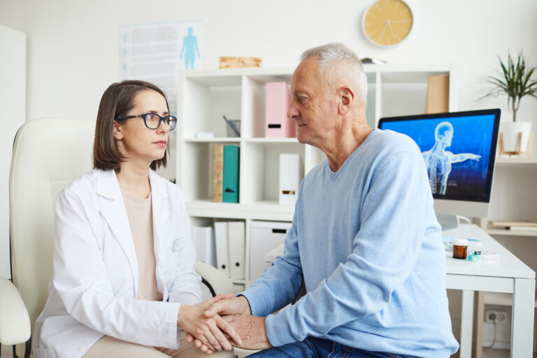 Portrait of caring female doctor holding hands with 50-60 year old senior patient while discussing diagnosis during preventative consultation